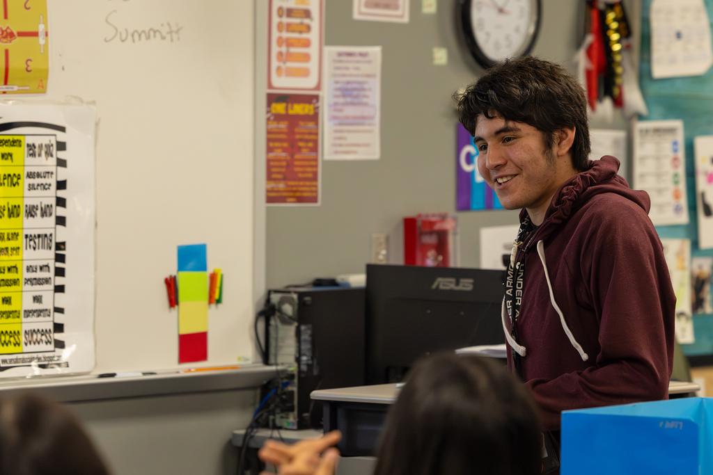 Student stands at desk speaking to class in a classroom.
