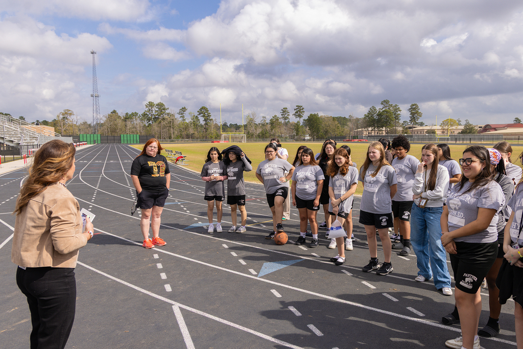 Board member speaks to group of students gathered on school track field.