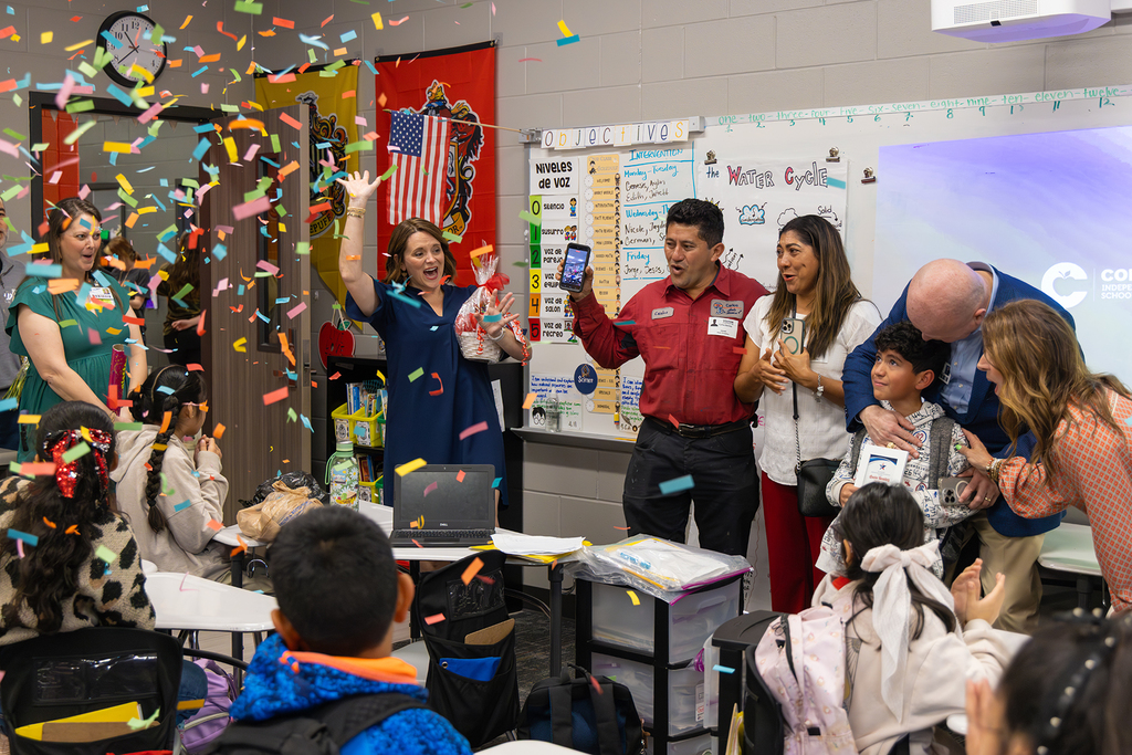 Students and staff celebrate in classroom as confetti falls during award surprise.