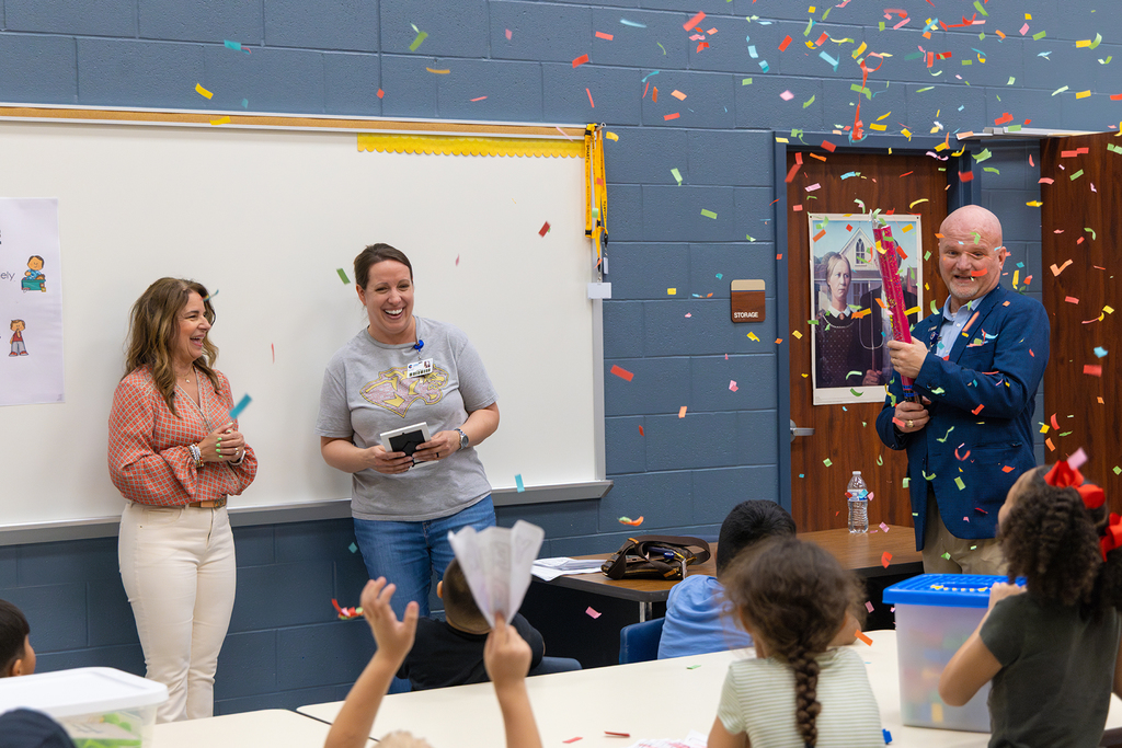 Staff celebrate teacher in classroom as confetti falls and students watch.