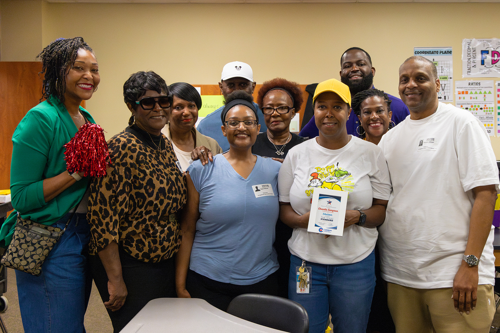 Group of staff pose together in classroom with educator holding recognition plaque.