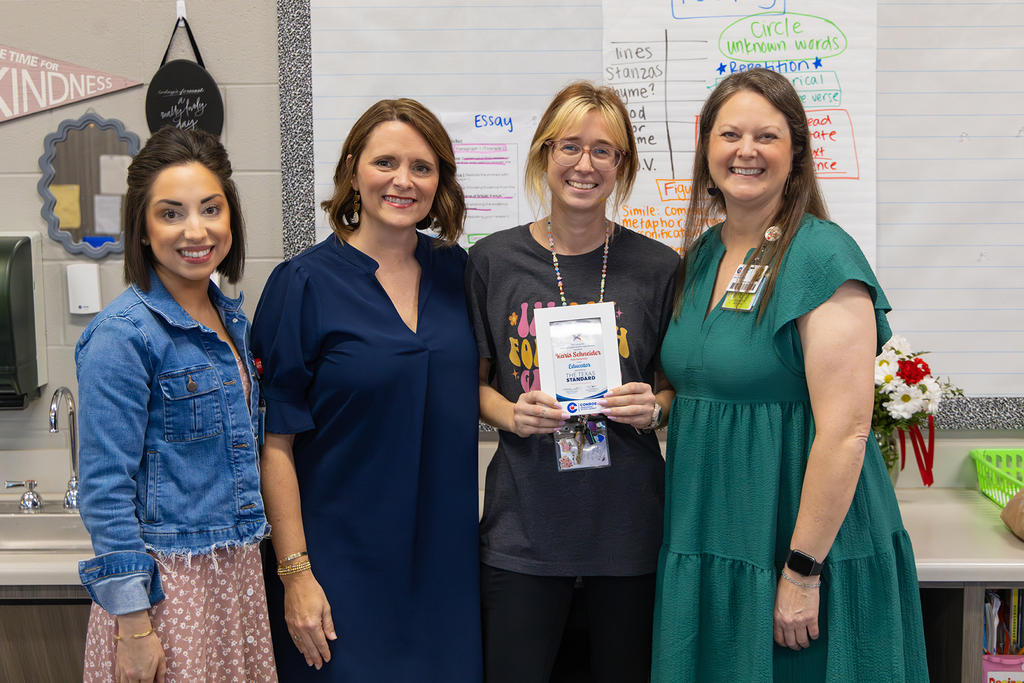 Four staff members pose in classroom with educator holding recognition plaque.