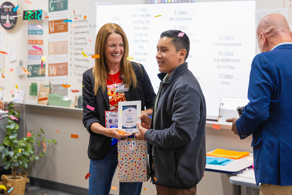 Student receives recognition plaque from board member in classroom as confetti falls.