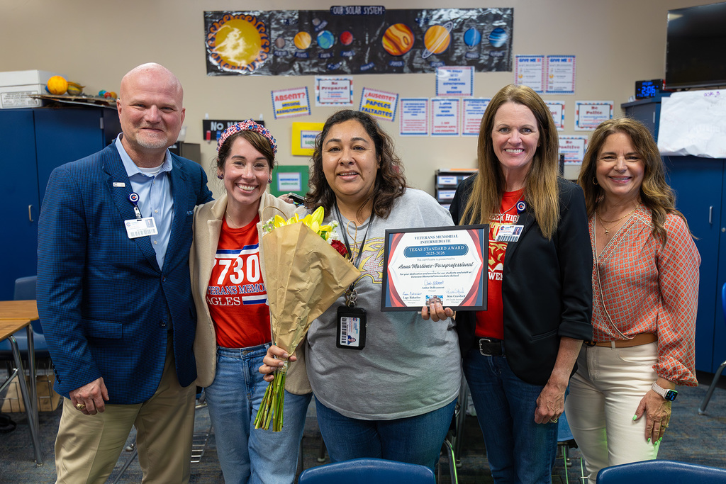 Staff pose in classroom with educator holding flowers and framed award.