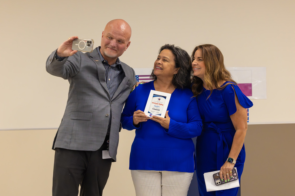 Superintendent takes selfie with board member and educator holding recognition plaque.