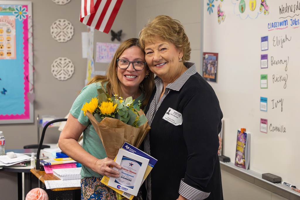 Educator with school namesake in classroom with flowers and recognition certificate.
