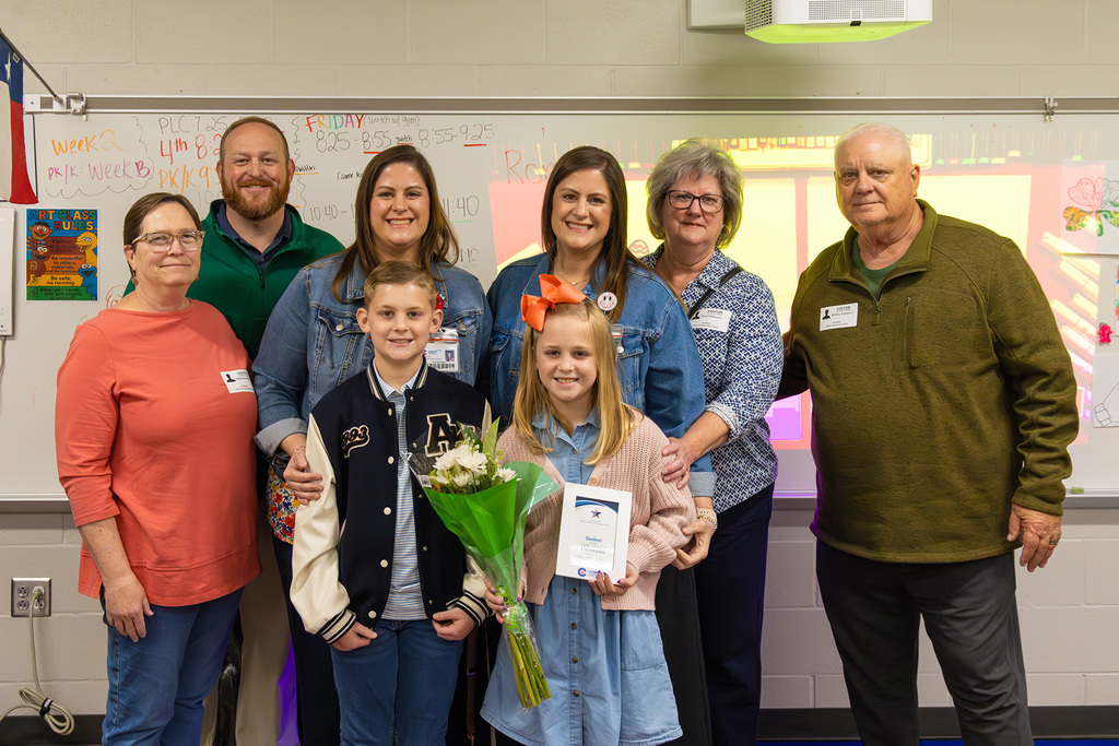 Family pose with student in classroom holding flowers and certificate.