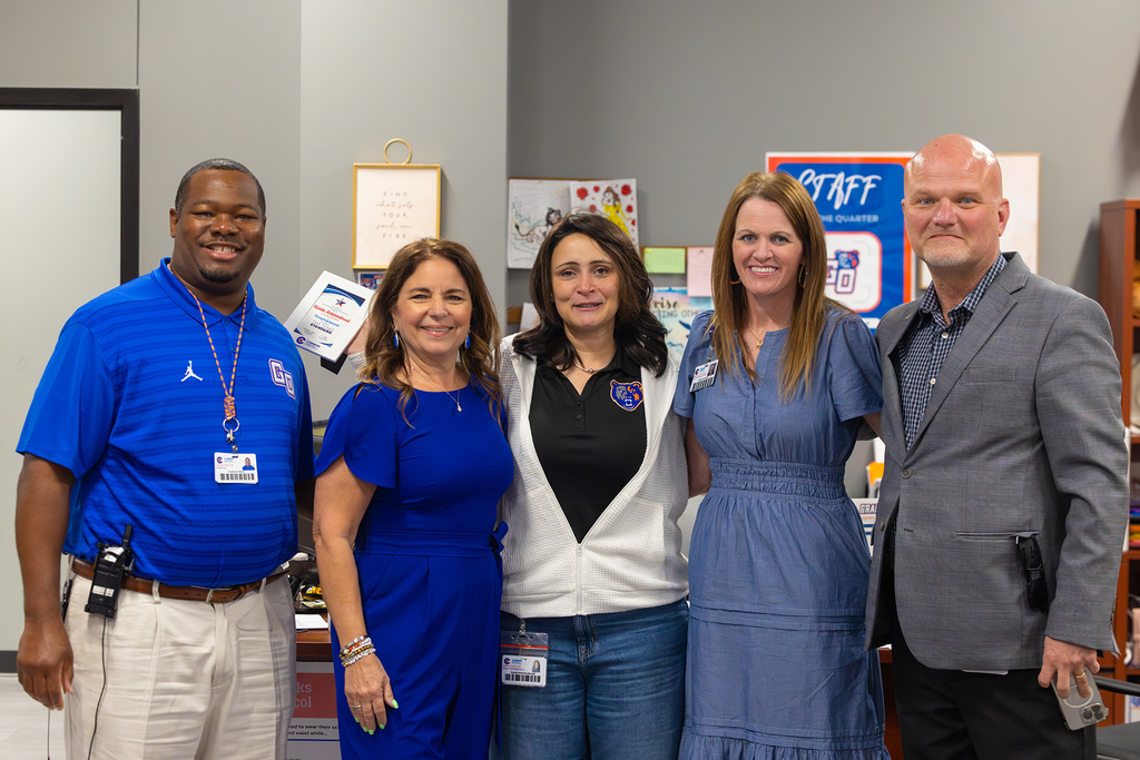 Group of staff pose together in office holding recognition certificate.