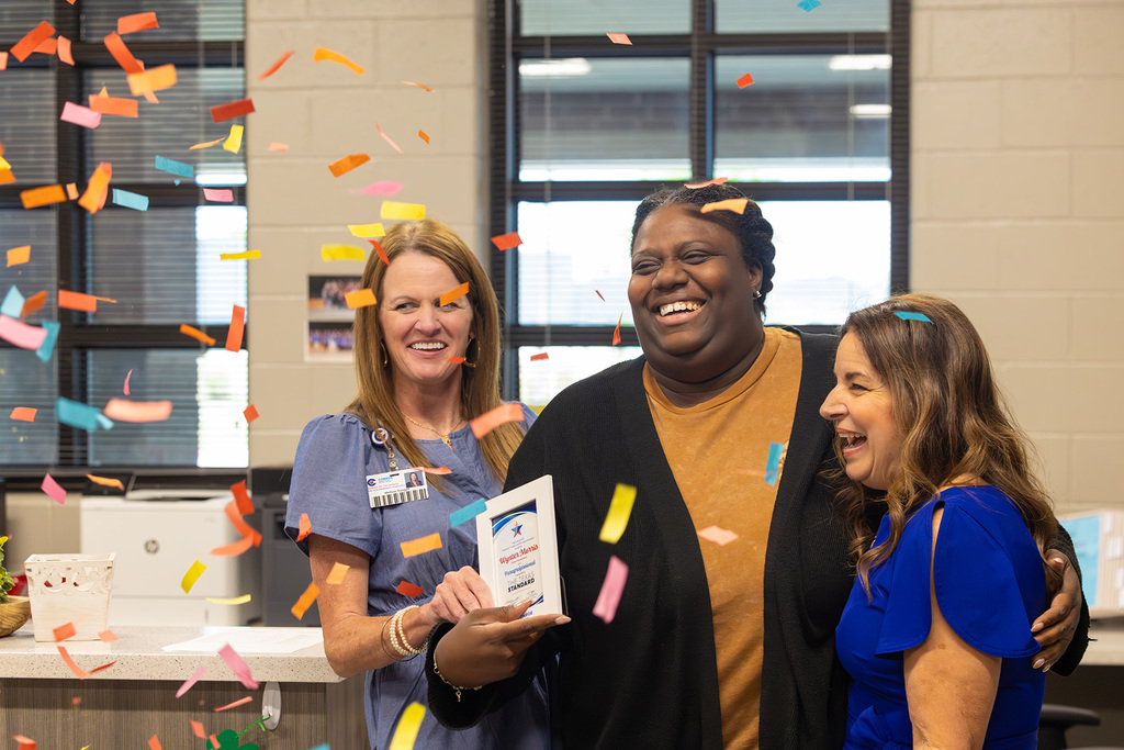 Board members celebrate with confetti as educator holds award and smiles.