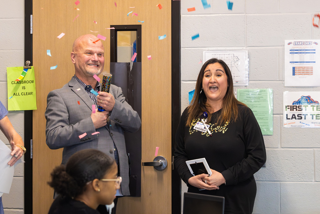Administrator pops confetti as staff member reacts with surprise in classroom.