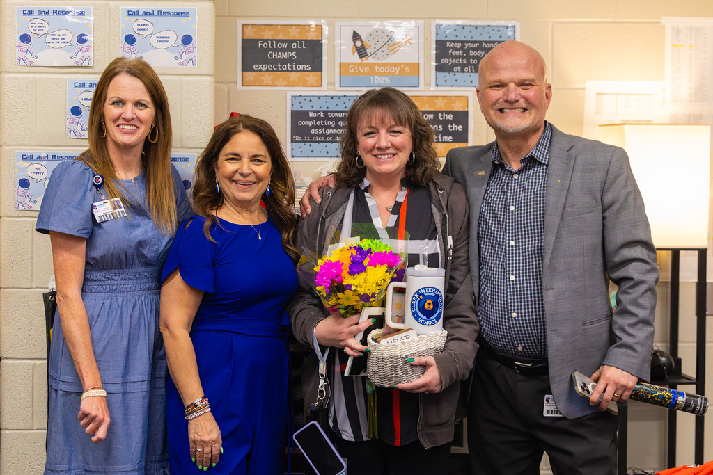 Group of staff pose with teacher holding flowers and gift basket.