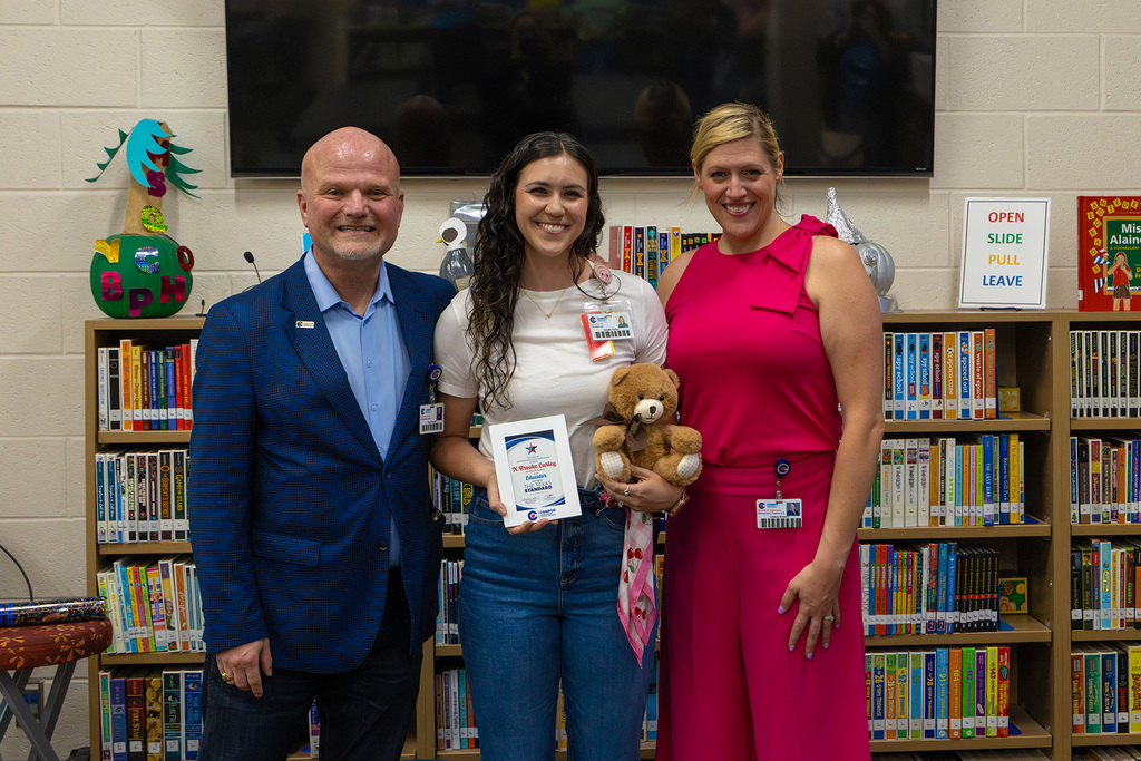 Superintendent and board member with educator holding certificate and stuffed bear.