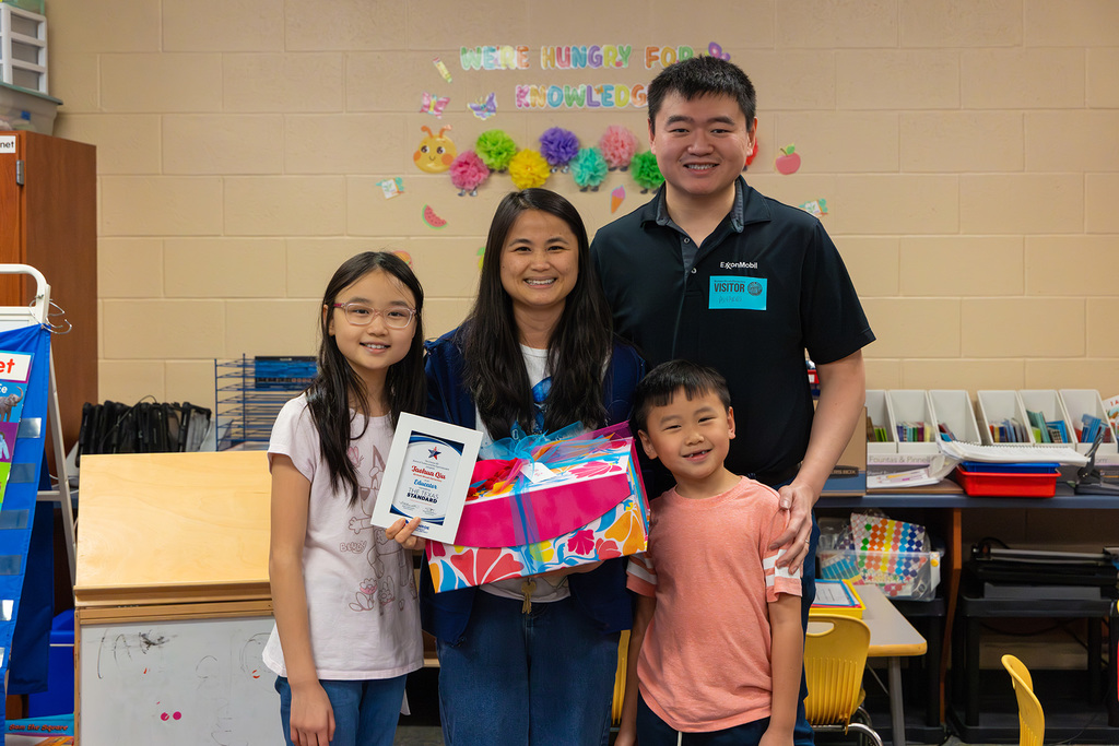 Educator stands with family holding certificate and gift box in classroom.
