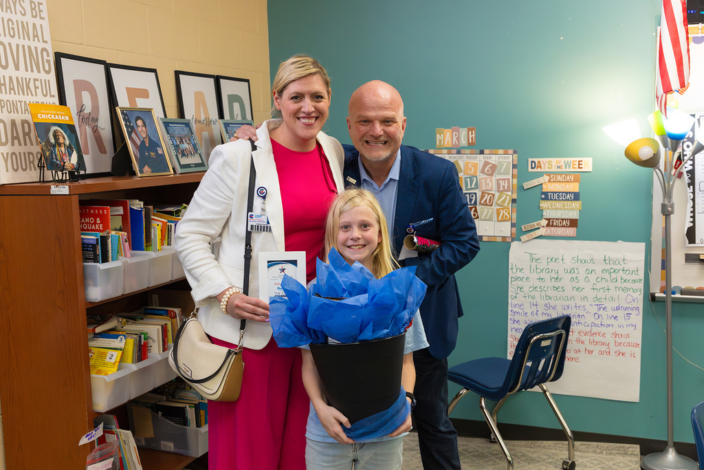 Student stands with board member and superintendent holding large bouquet and recognition certificate.