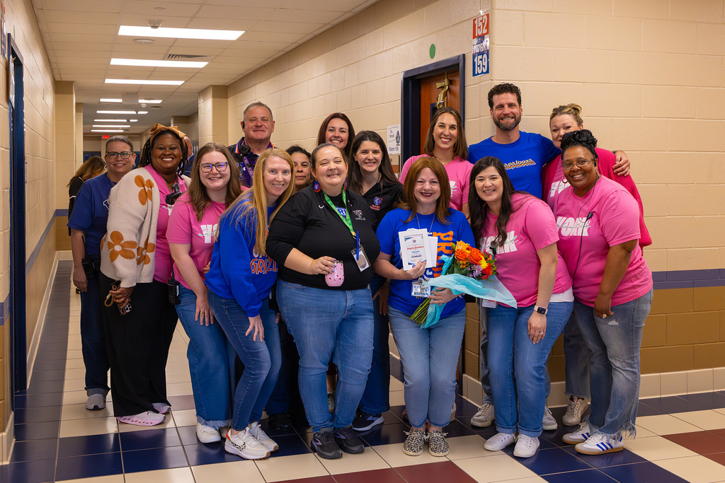 Large group of staff pose in hallway with educator holding flowers.