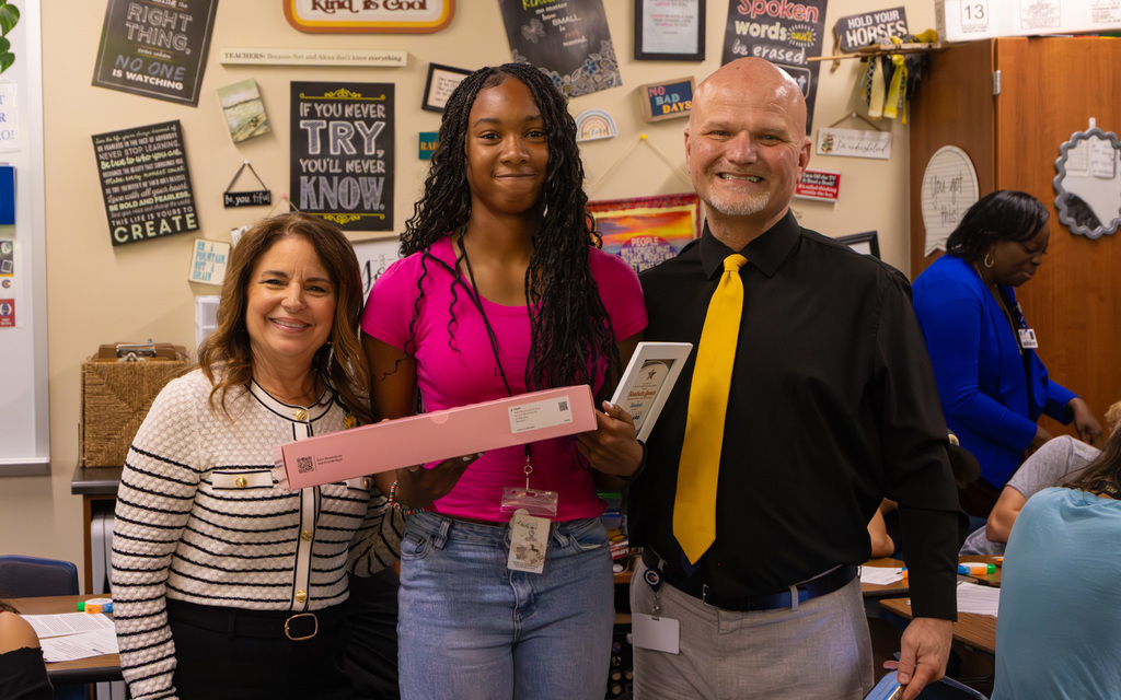 Three individuals stand side by side in a classroom adorned with various motivational signs