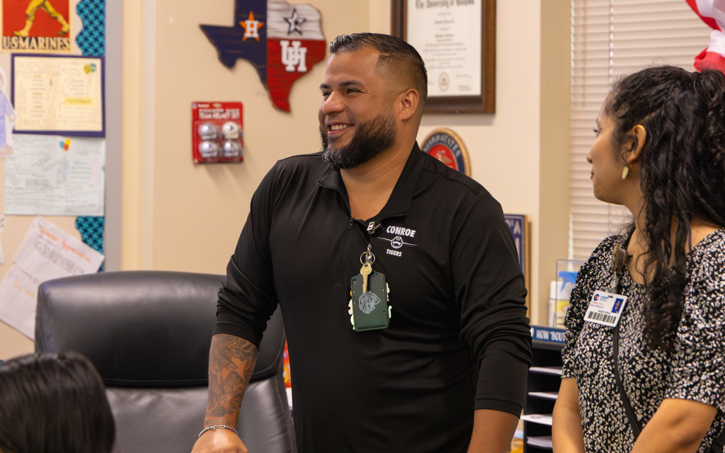 Two colleagues interacting in an office, one man wearing a black shirt with keys and a woman listening attentively