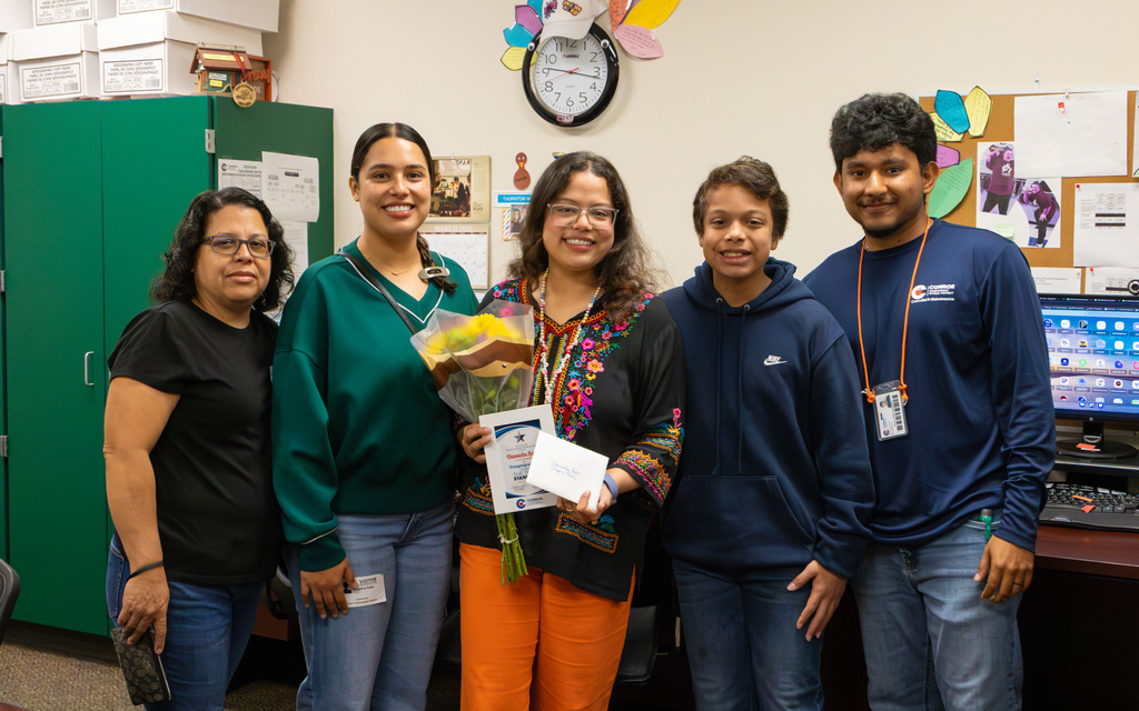 Group of five individuals posing for a photo featuring a woman holding a bouquet and award
