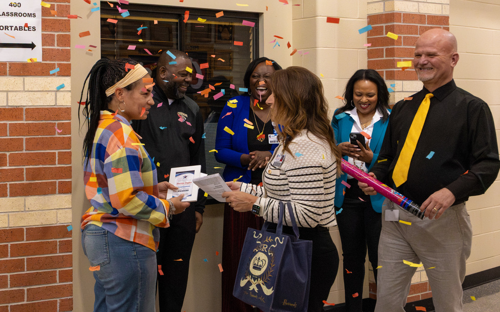 Board member handing out a recognition award to a school staff member while confetti falls around them in a festive moment.