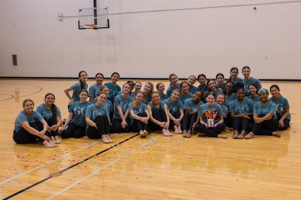 Golden girls in matching shirts on a gym court floor, with one girl holding a candy bouquet.
