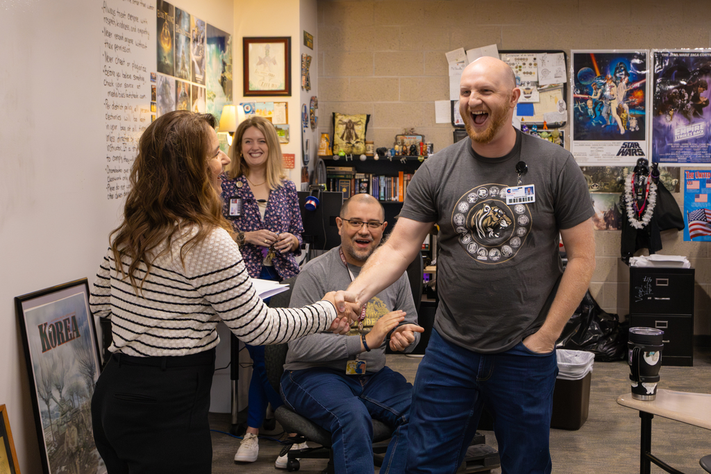 In a room adorned with Star Wars posters, a man and woman engage in a handshake as two colleagues watch