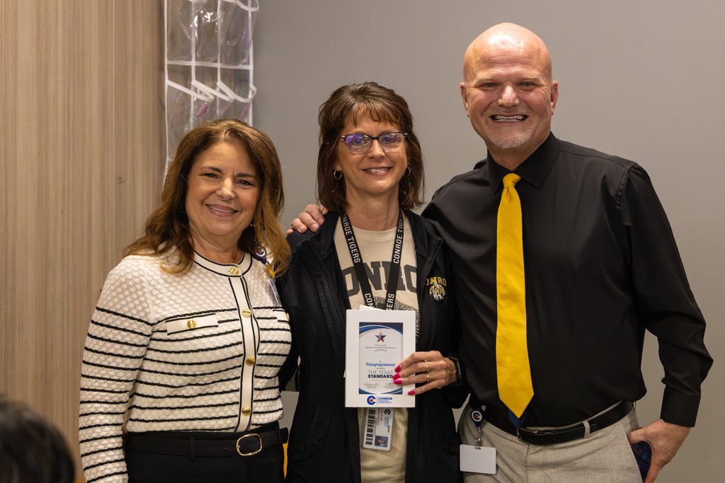 Three individuals side by side, the woman in the center holding a recognition certificate, smiling for a photo