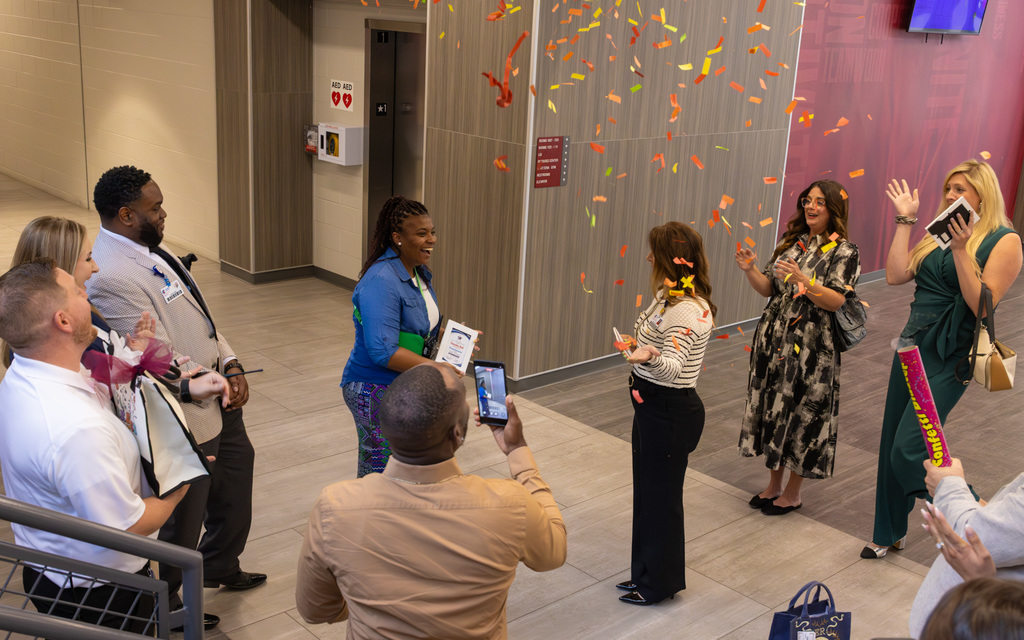 A person receives an award indoors as a crowd cheers, and one person records with a phone amidst falling confetti