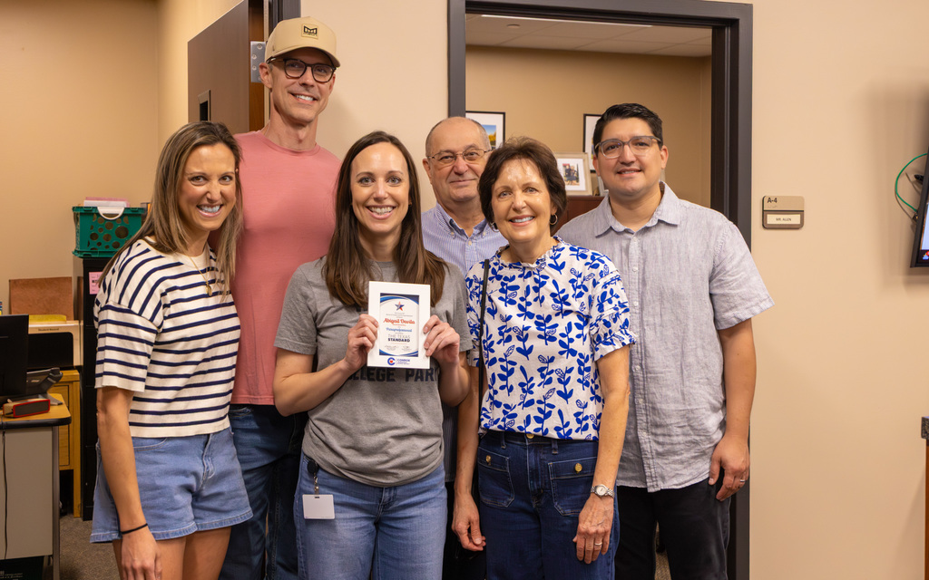 Six people posing inside an office doorway, with one person displaying an award