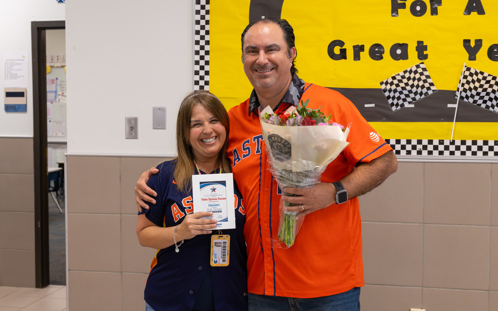 Two people stand together, with one holding a framed certificate and the other holding flowers