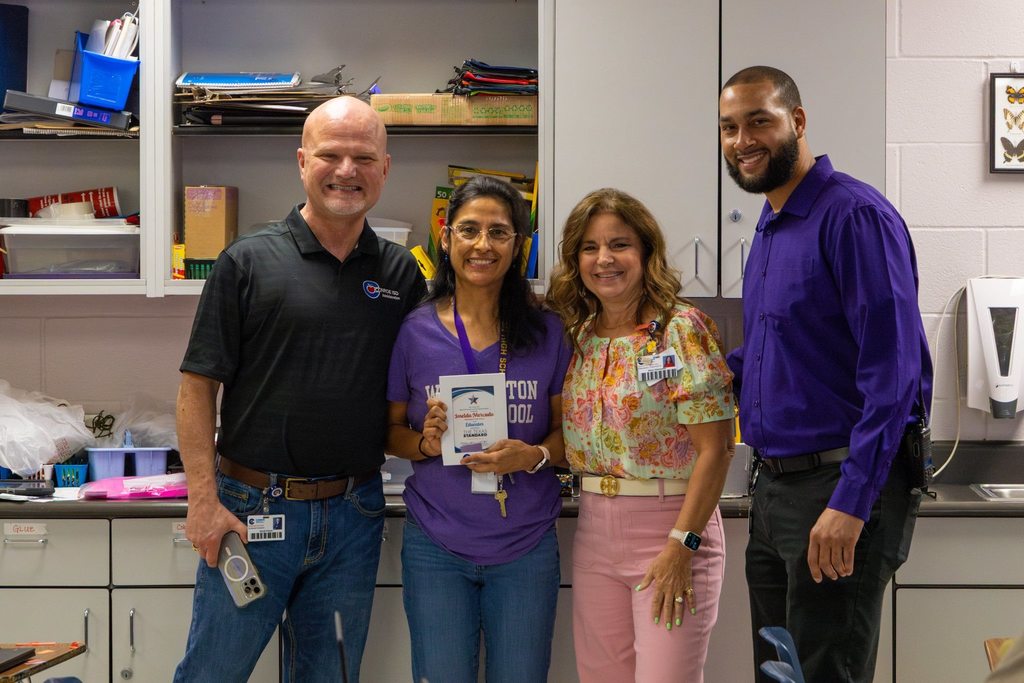 Superintendent, Board President and Principal with staff member holding award plaque.