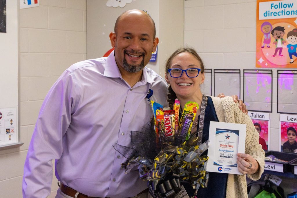 Principal with staff member holding award and candy bouquet.
