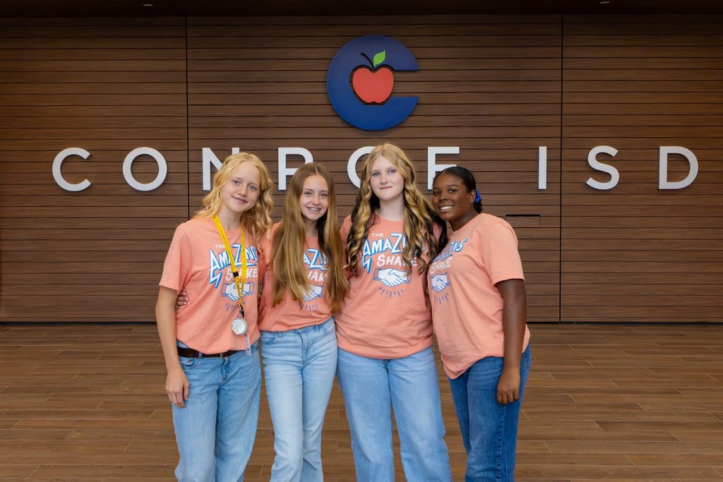 Four girls in matching orange shirts in front of district logo.