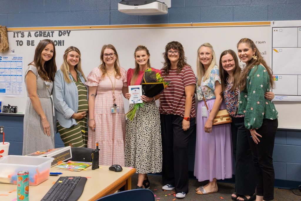 Teachers with colleague holding award plaque and flowers.