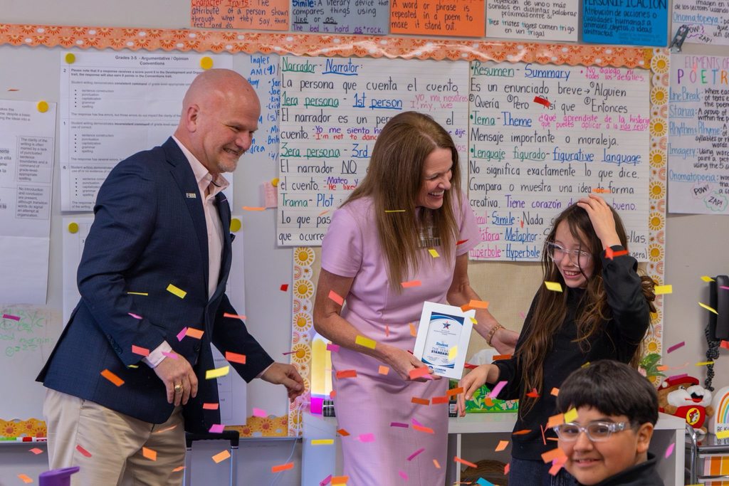 Superintendent and board member present student with award plaque while confetti falls.
