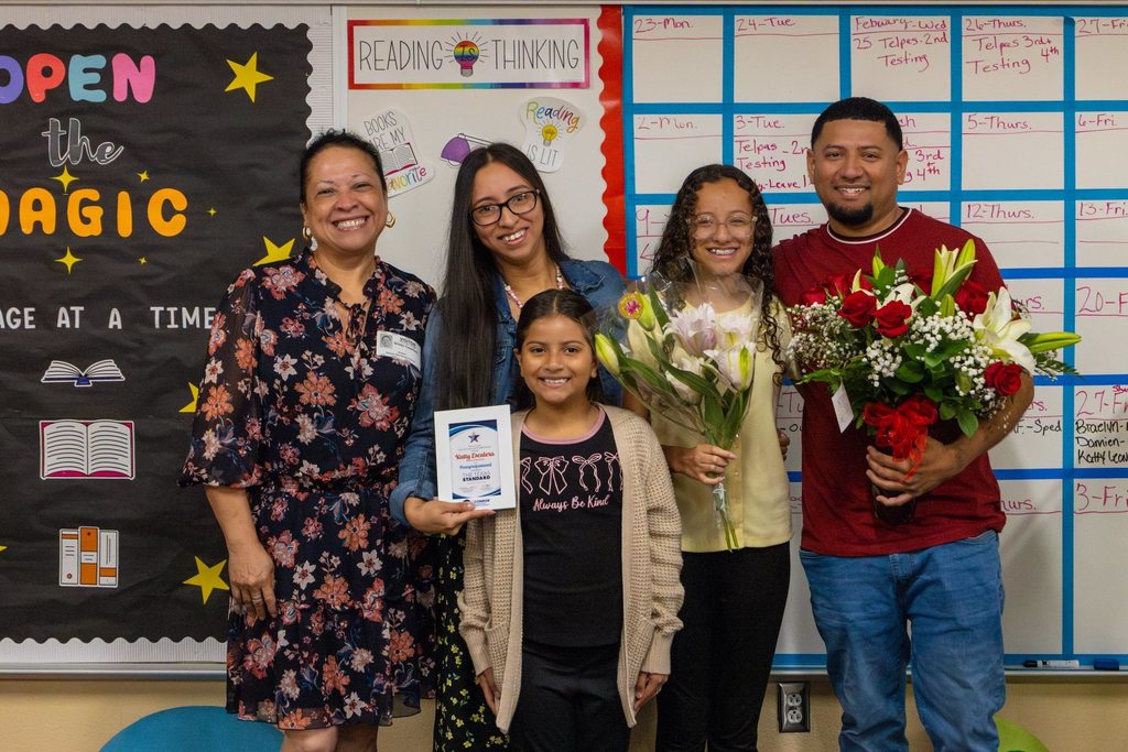 Staff member with award plaque joined by family holding flowers.
