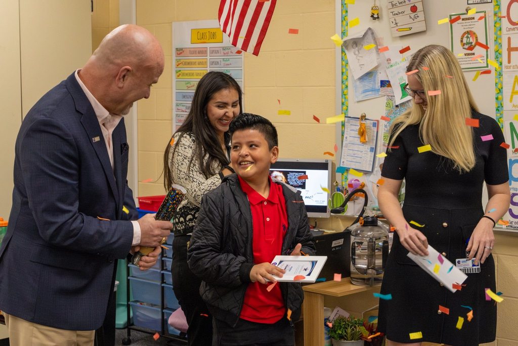 Superintendent pops confetti while board member congratulates student with award plaque.