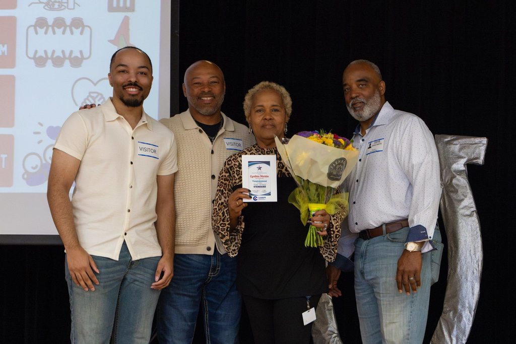 Staff member with award plaque and flowers joined by family.