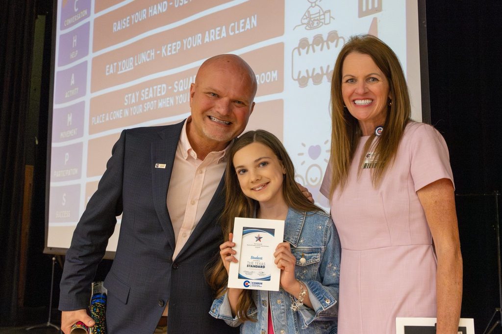 Superintendent and board member with student holding award plaque.