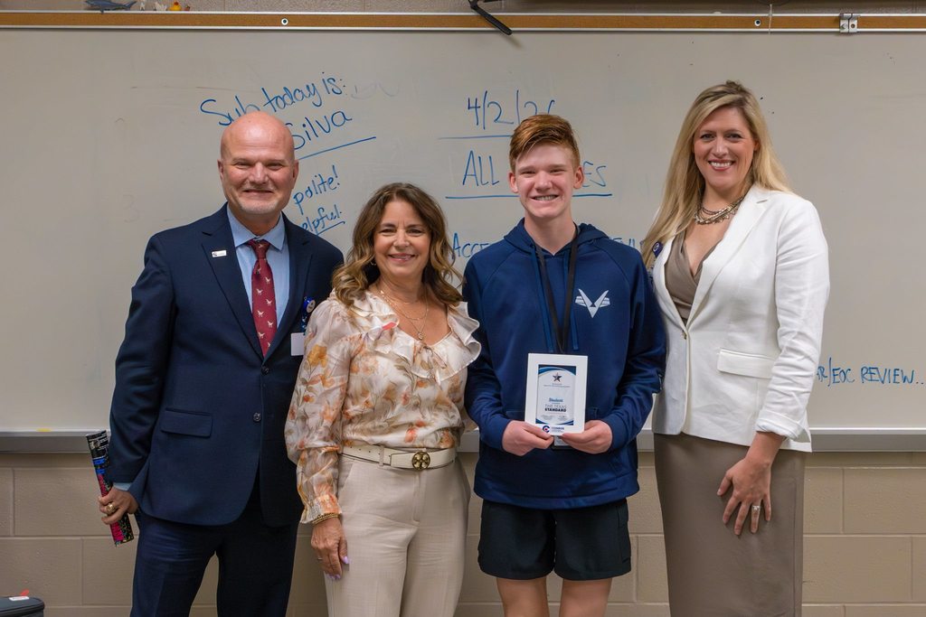 Superintendent and two board members congratulate student with award plaque.