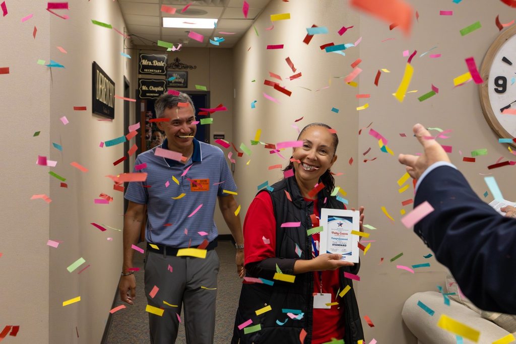 Staff member with award plaque joined by family as confetti falls.