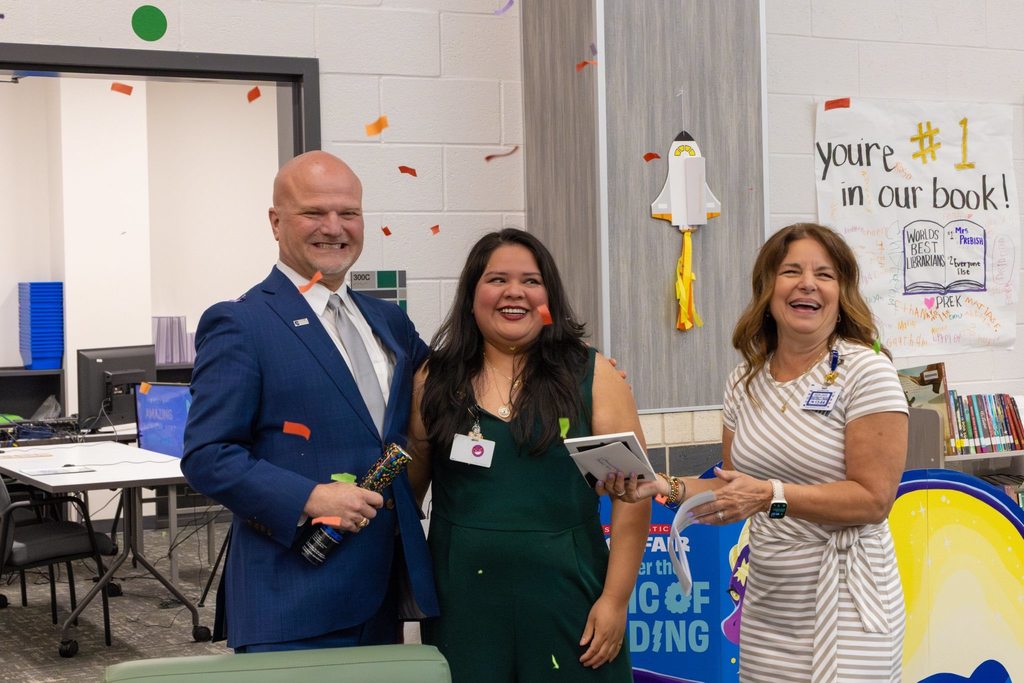 Superintendent and Board President present staff member with award as confetti falls.