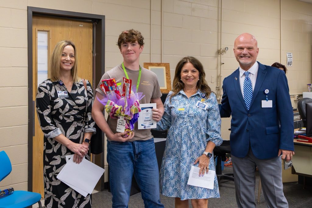 Superintendent and two board members present student with award plaque and candy bouquet.