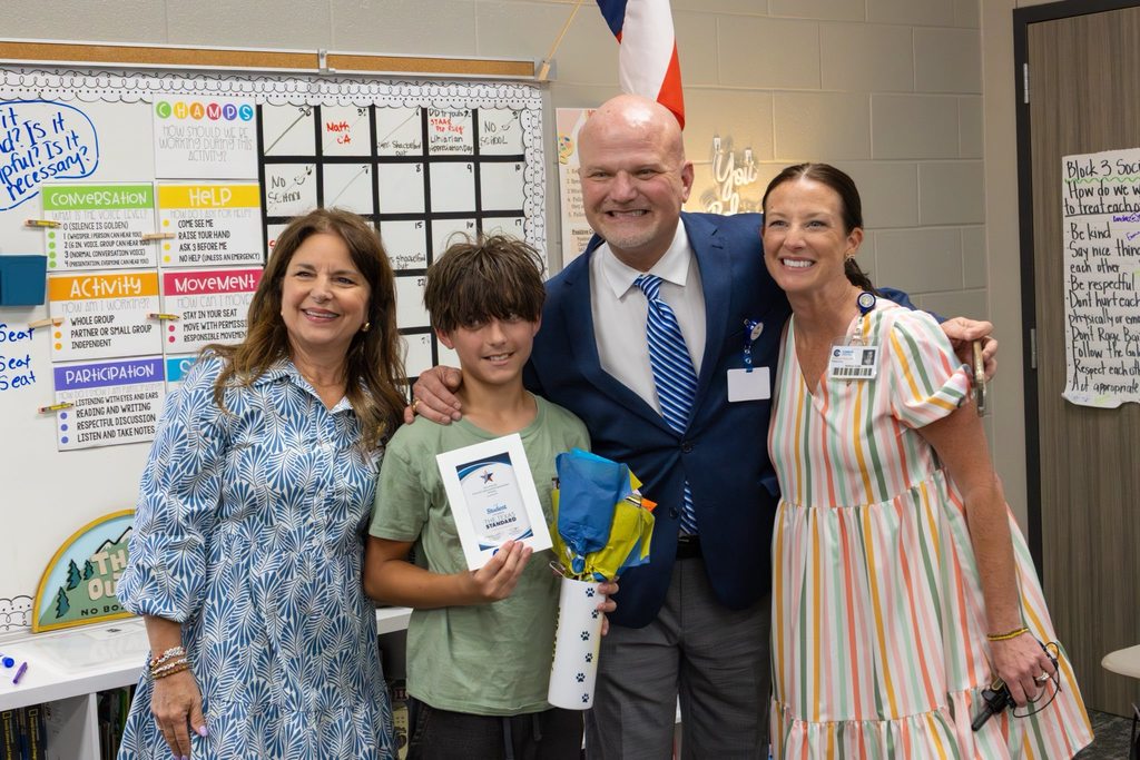 Superintendent, Board President and Principal congratulate student with award plaque and gift.