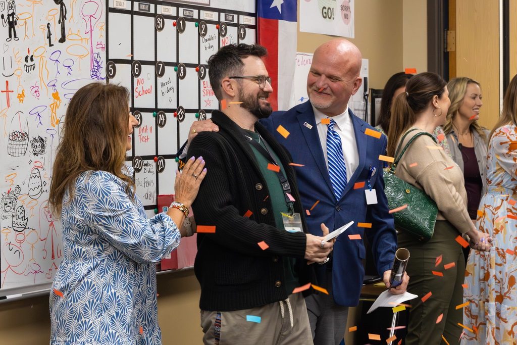 Superintendent and Board President congratulate staff member as confetti falls.