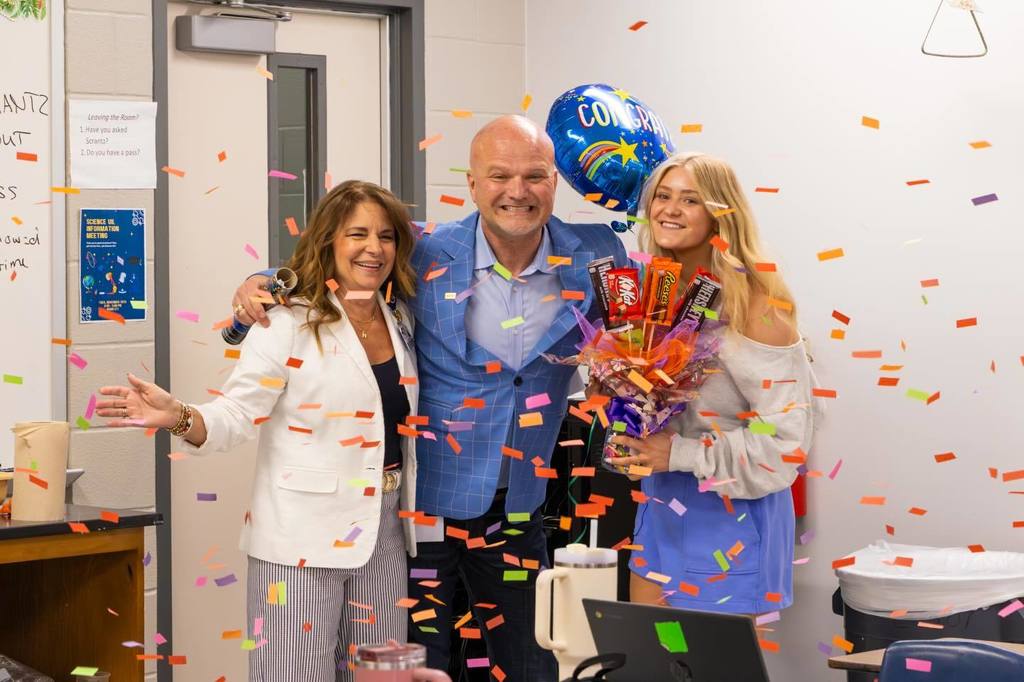 Superintendent and Board President congratulate student as confetti falls.