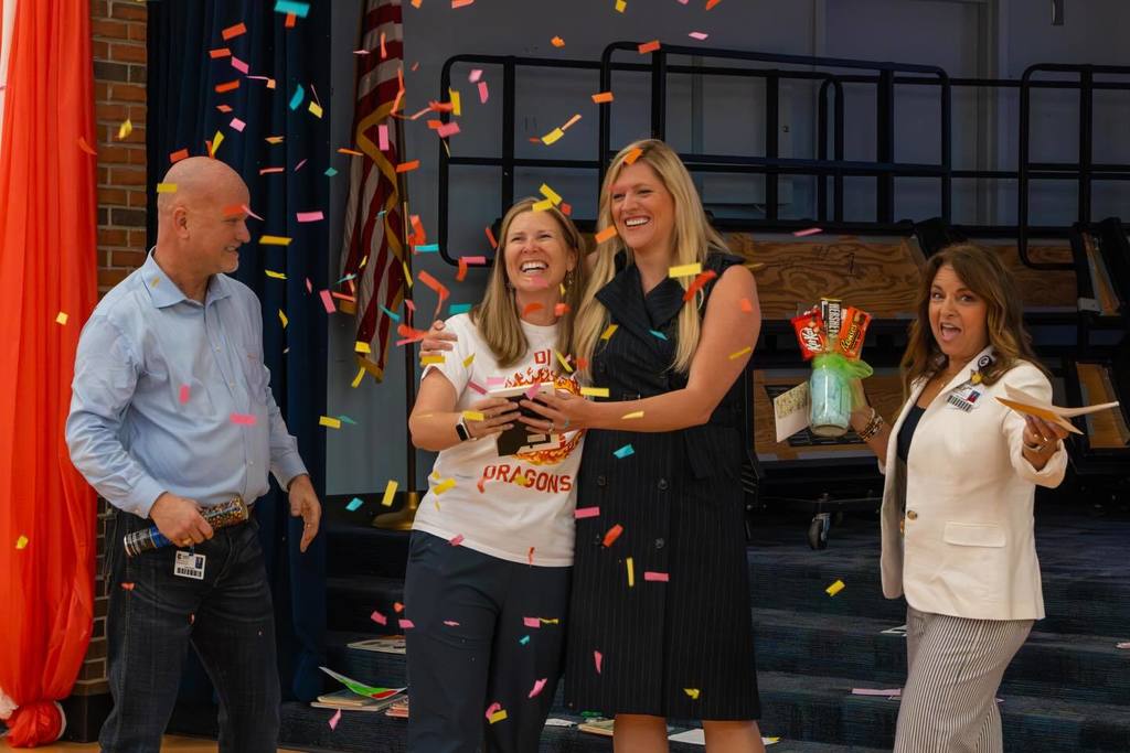 Superintendent and two board members congratulate staff member while confetti falls.
