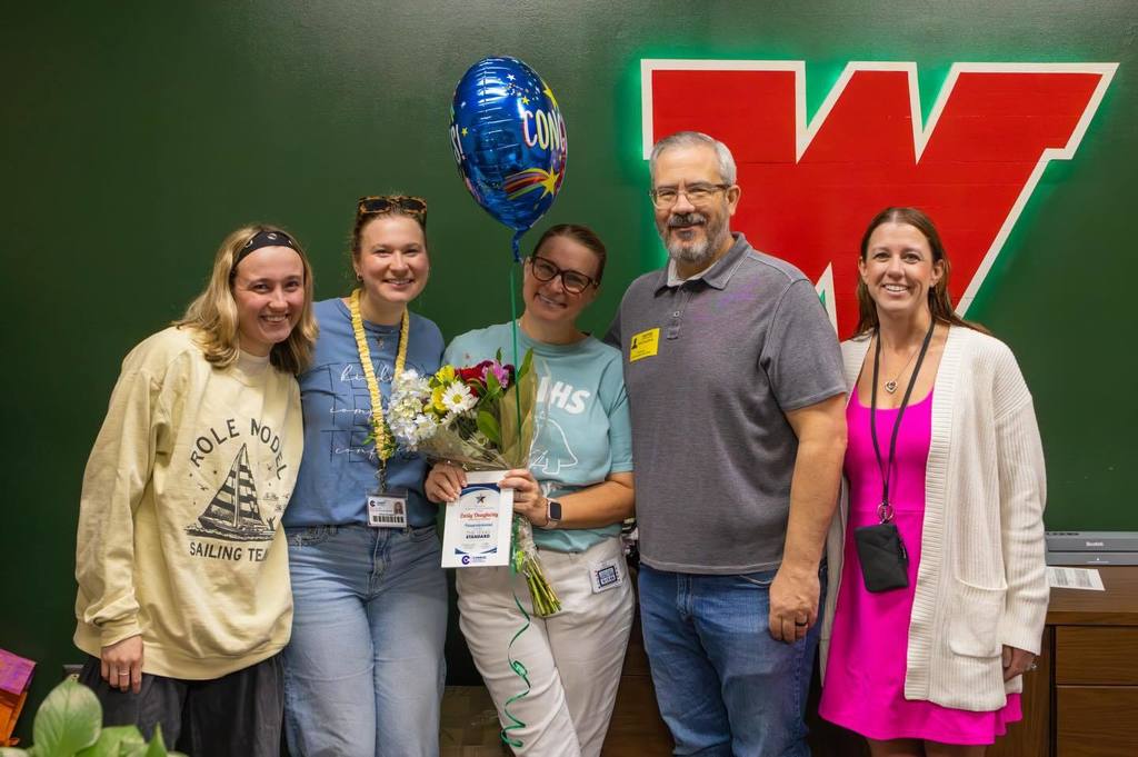 Staff member holding award plaque, flowers and balloon joined by family.