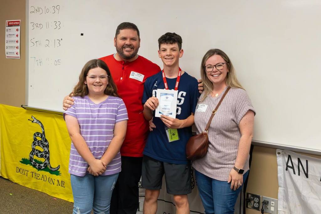 Student holding award plaque joined by family.