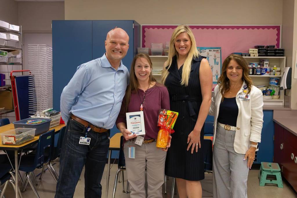Superintendent and two board members congratulate staff member with award plaque and candy bouquet.