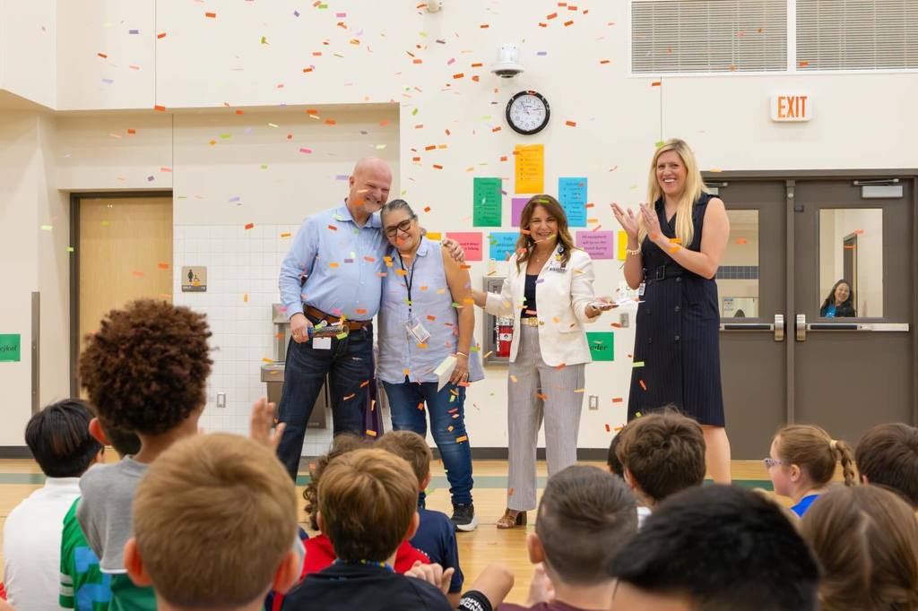 Superintendent and two board members congratulate staff member as confetti falls.